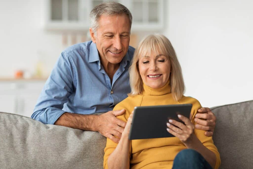Smiling Older Couple Using Tablet Computer Watching Movie Online Indoor